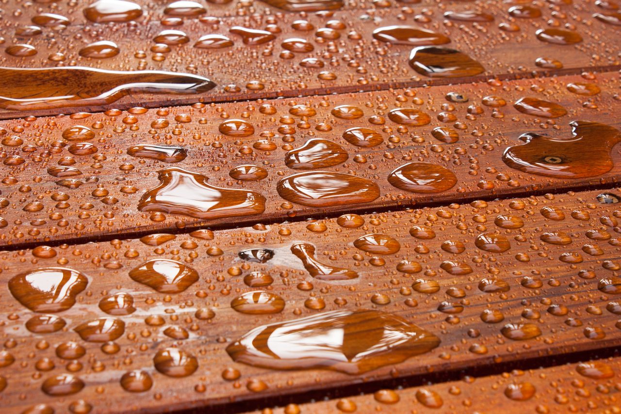 A closeup on a recently sealed cottage deck just after the summer rain.  Water beads up in reflective pools as the sun begins to shine.