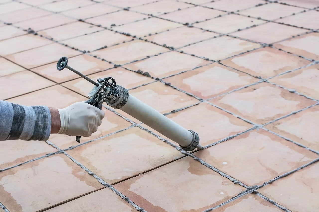 Applying silicone on the cracks of a tiled floor.