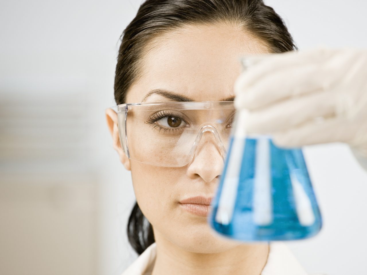 Female scientist looking at beaker of liquid.