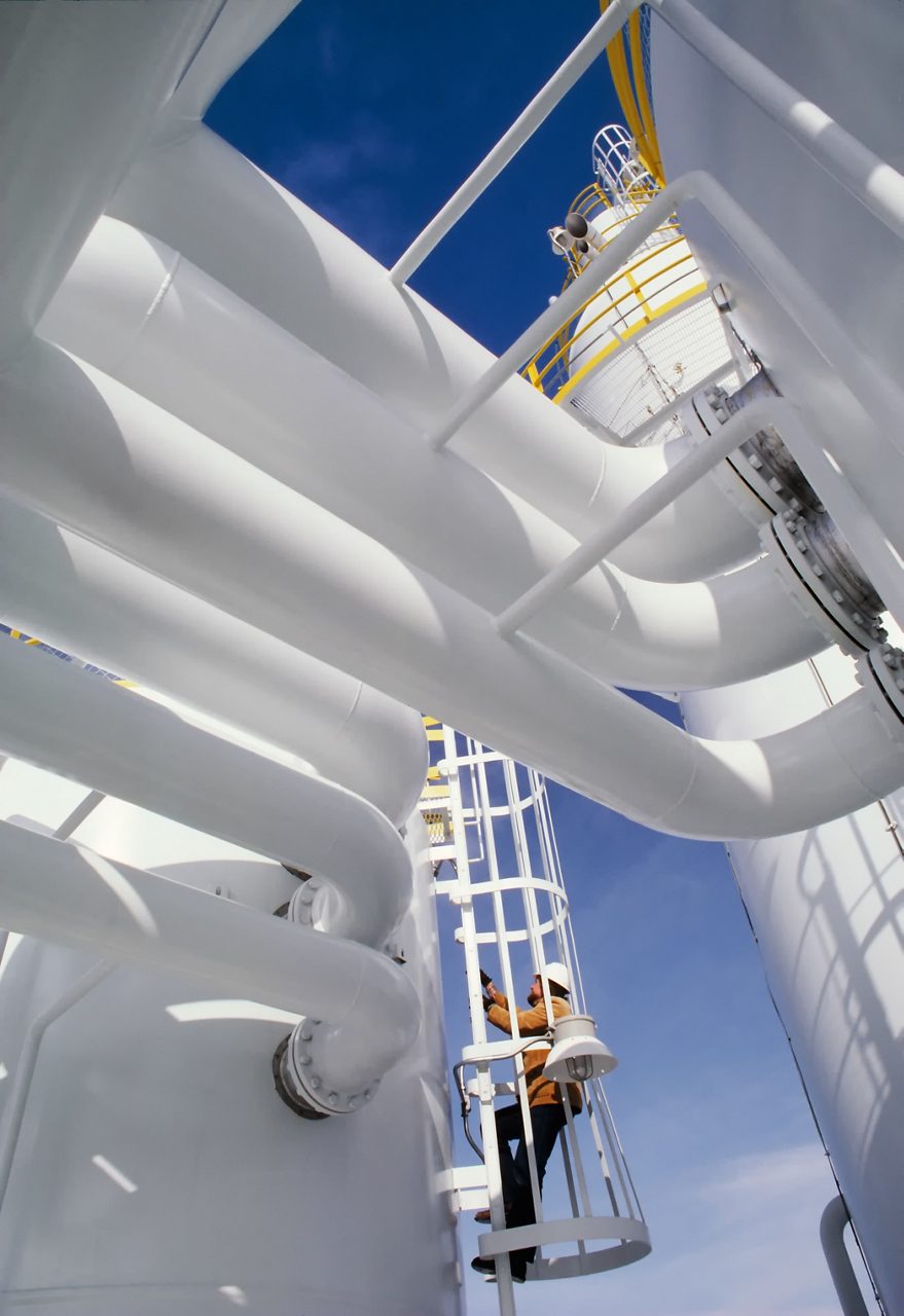 Industrial worker climbing a ladder at oil plant 