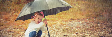 happy baby girl with an umbrella in the rain runs through the puddles playing on nature