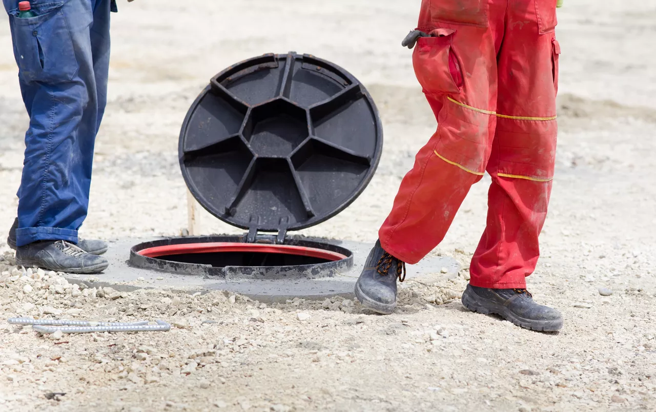Construction workers standing beside manhole with open cover at building site