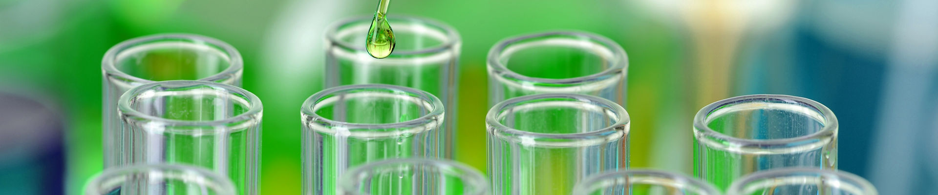 Green liquid dripping from pipette into laboratory test tubes