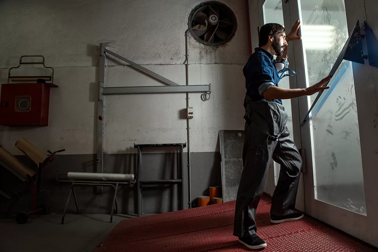 Man looking through glass door in factory setting.