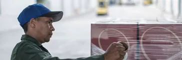 Factory worker wrapping pallet in plastic wrap at packaging factory