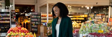 Woman placing blue plastic package into a Plastic Only recycle bin at the grocery store.