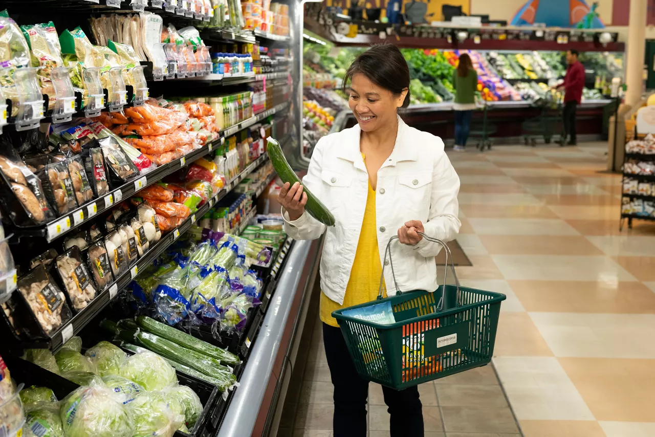 Shopper selecting a plastic wrapped cucumber at the grocery store