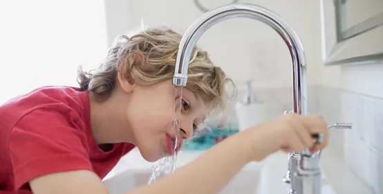 Boy drinking water from bathroom faucet