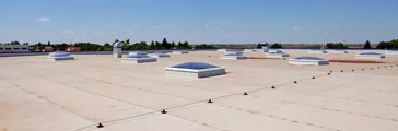 Flat roof with skylight and hydro insulation membranes under a blue sky with few clouds.