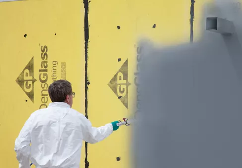 Man spraying AirBarrier system, DefendAir, on a wall outside. From Mark Boardman video for Build A Better System