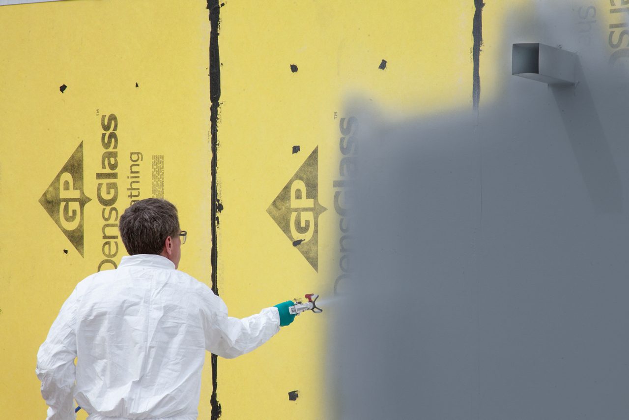 Man spraying AirBarrier system, DefendAir, on a wall outside