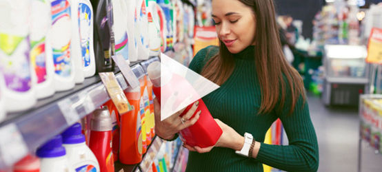 Jovem dona de casa lendo informações sobre a garrafa de detergente no supermercado.