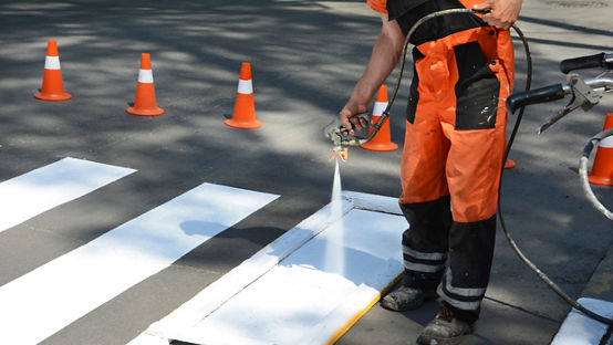 O trabalhador está pintando uma faixa de pedestres. 