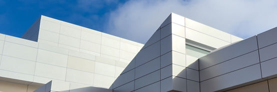 Commercial external metal composite panels on a building with blue sky and clouds in the background. The durable metal composite panels are two shades of grey in color on the modern building.