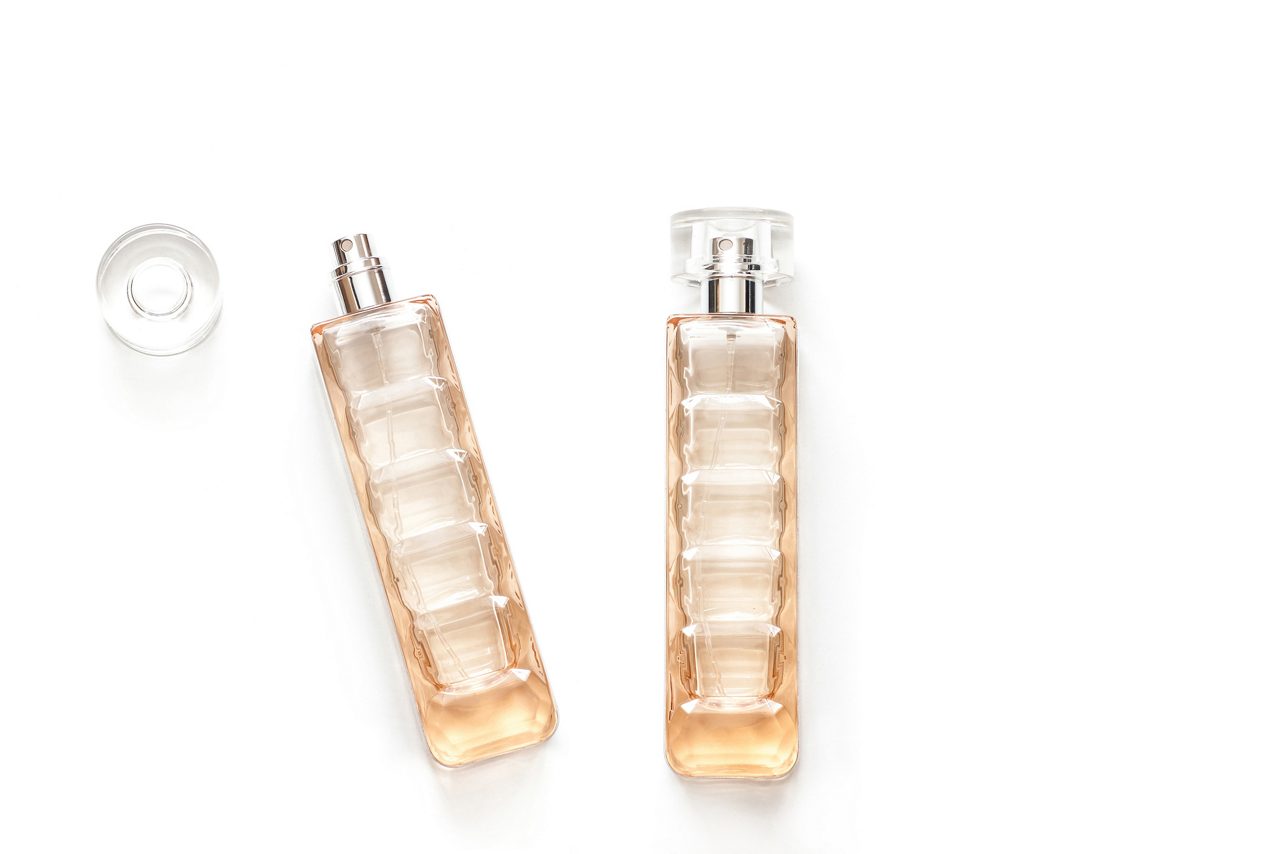 Two perfume bottles, transparent glass spray and bottle cap isolated on white background