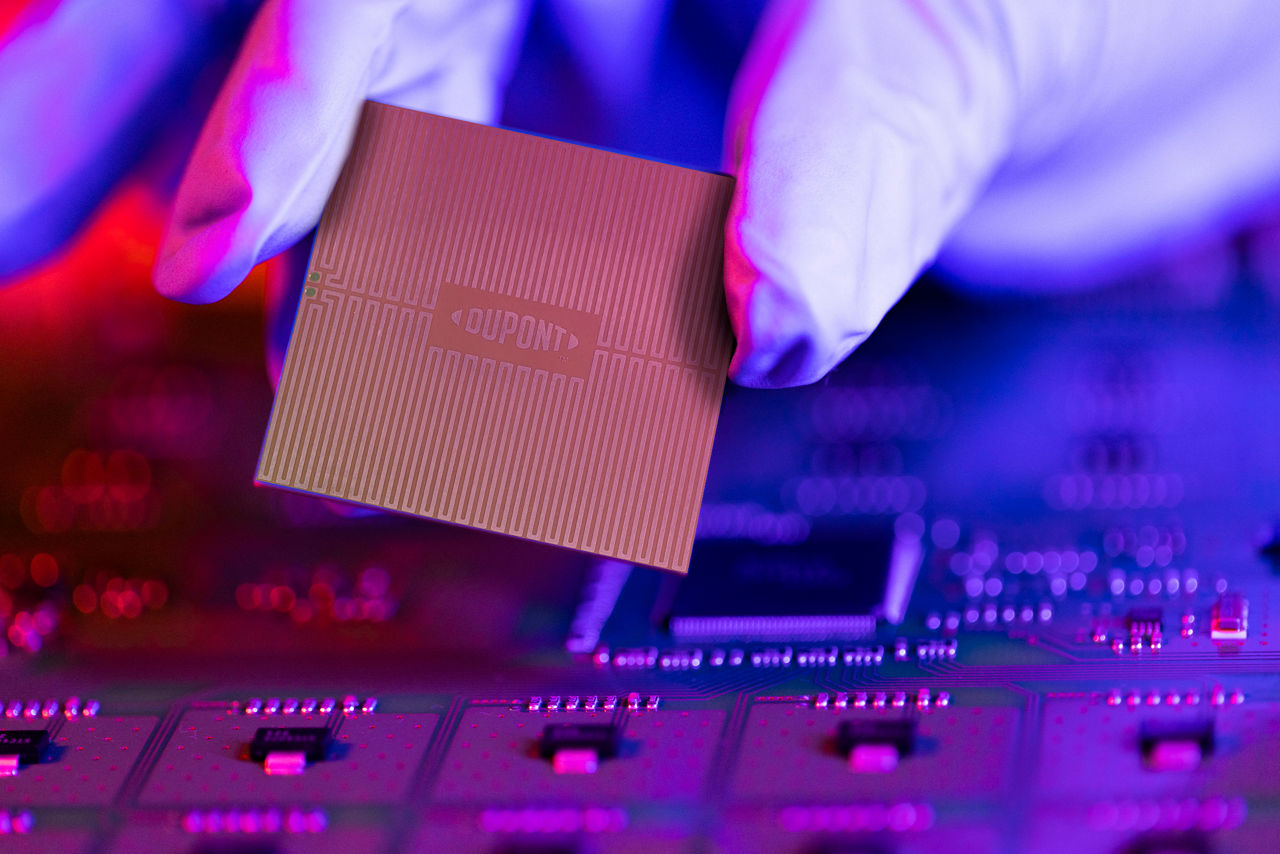 The engineer's gloved hand is holding the CPU chip against the background of the motherboard.