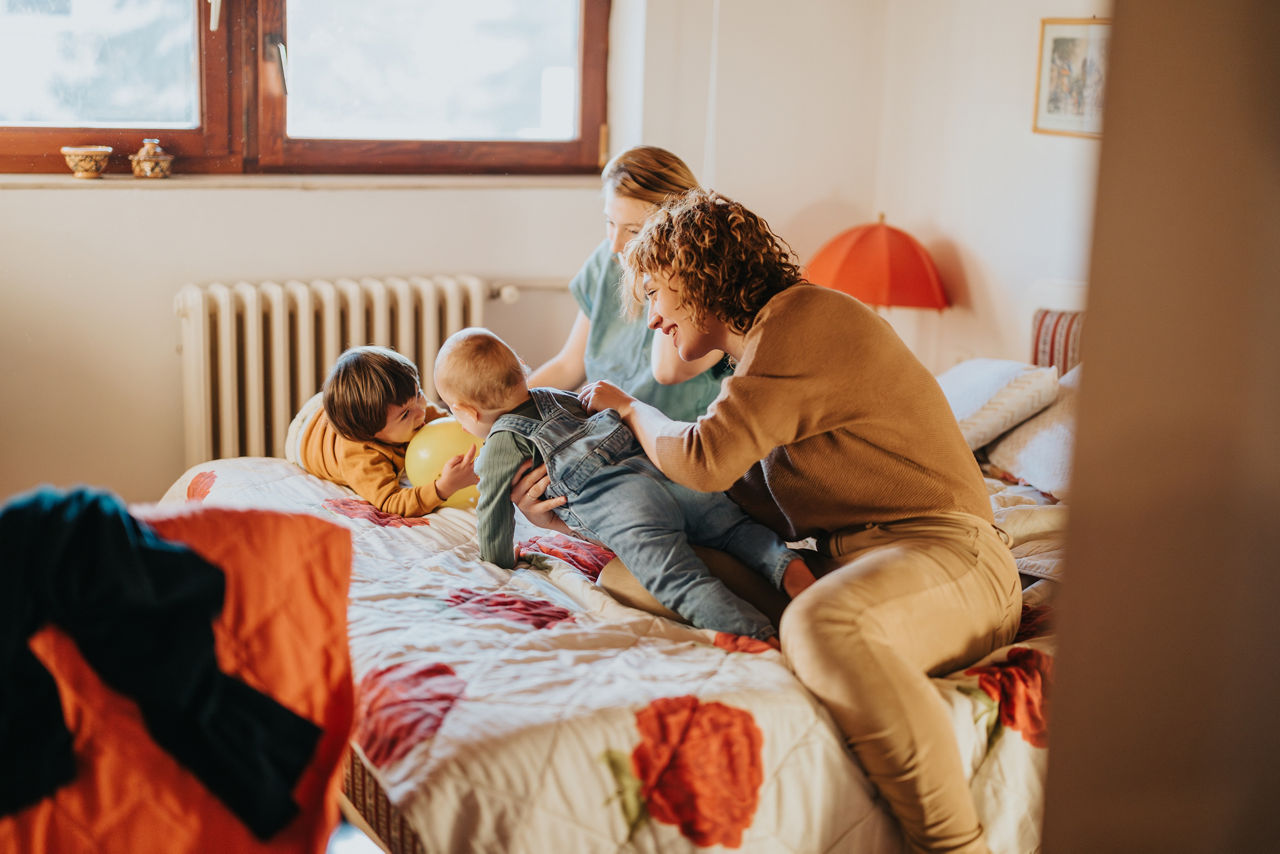 A joyful moment of a family playing with their children on a bed in a warm, inviting environment, emphasizing family bonds and care.