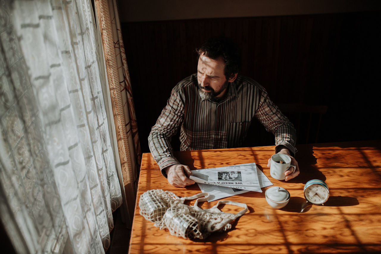 Portrait of poor despaired man sitting at table drinking tea. Old house interior.