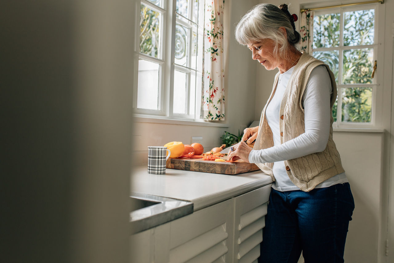 Senior woman preparing food in kitchen. Woman cutting vegetables on a chopping board standing in kitchen.