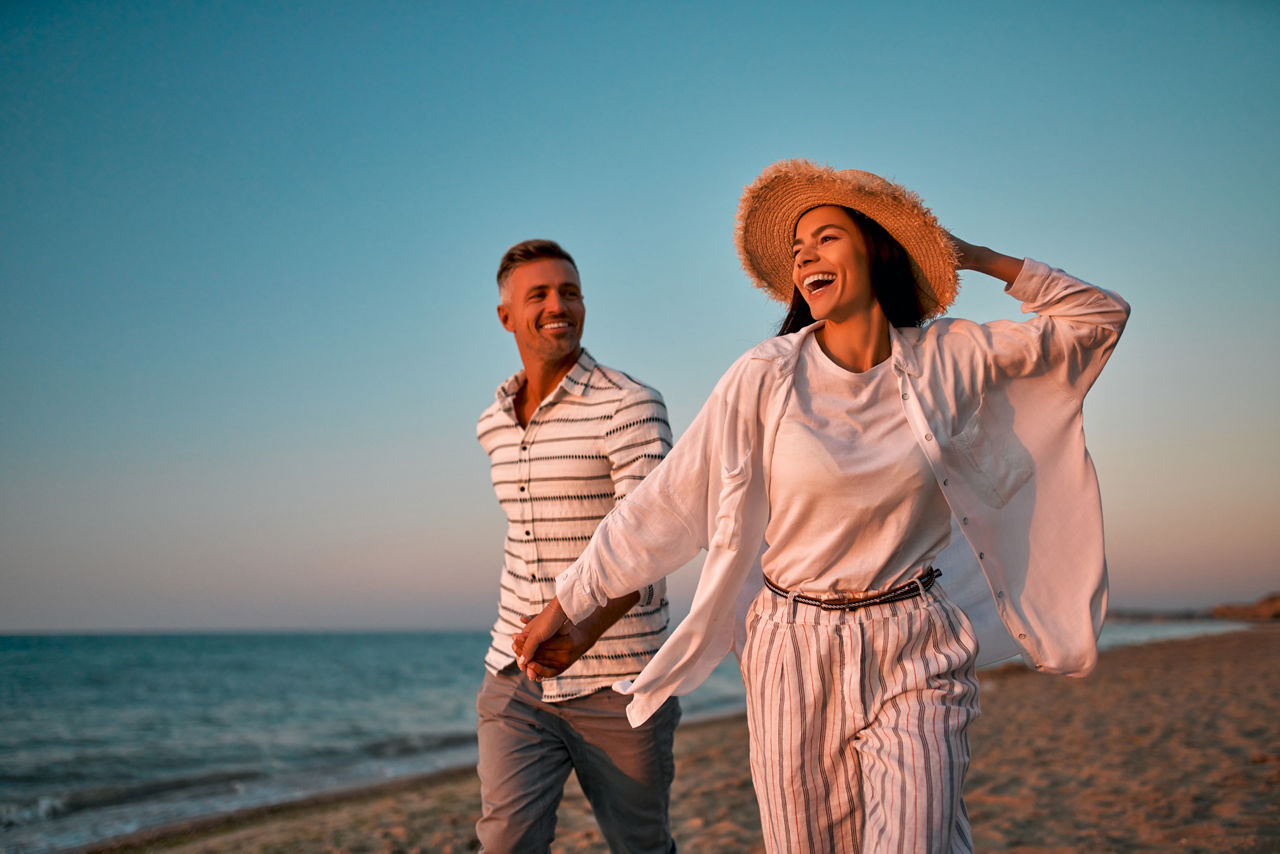 Couple on the beach. Traveling together to the sea. Handsome man and beautiful woman walking on the seashore and holding hands