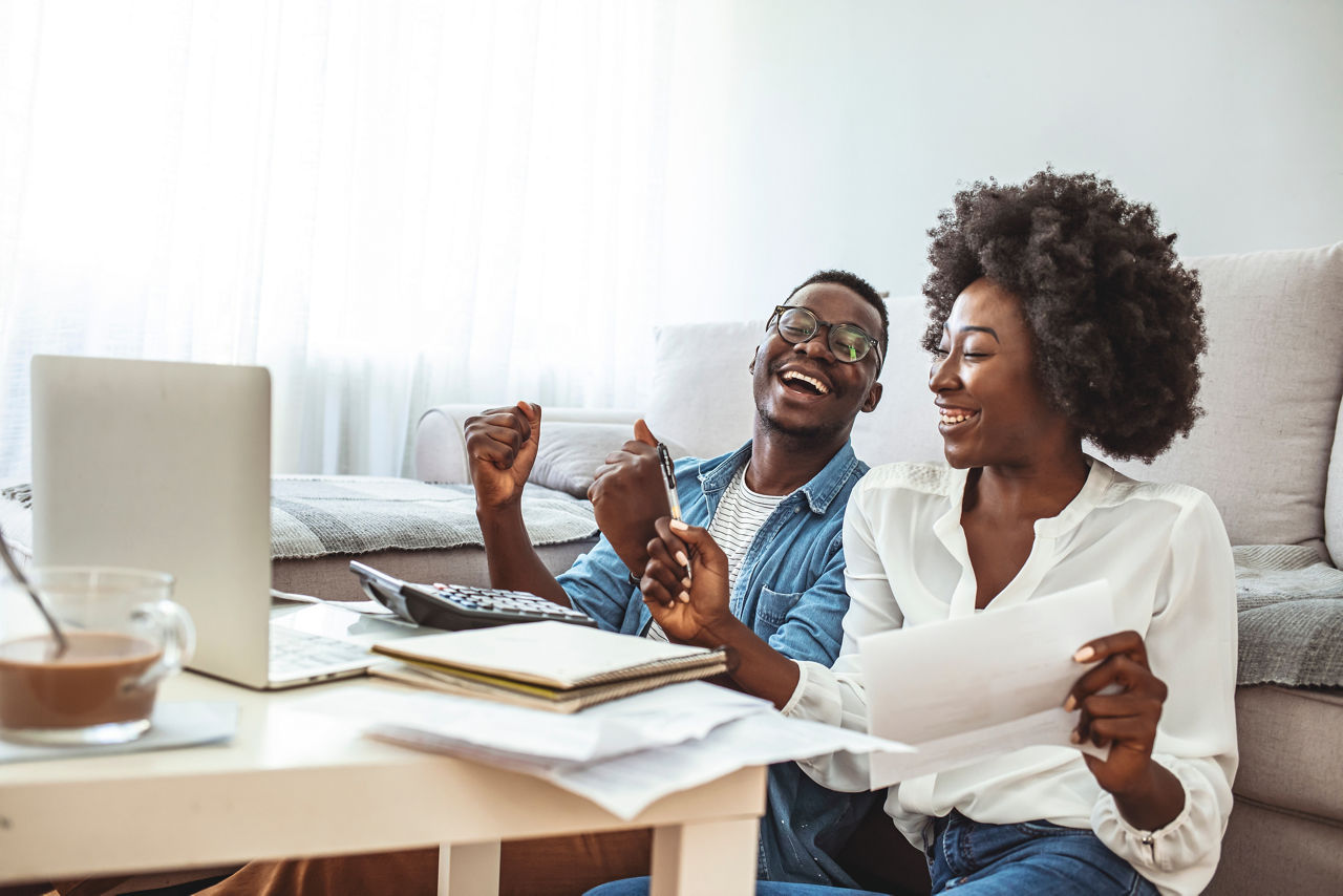 Photo of cheerful loving young couple using laptop and analyzing their finances with documents. Look at papers. Happy couple at home paying bills with laptop

