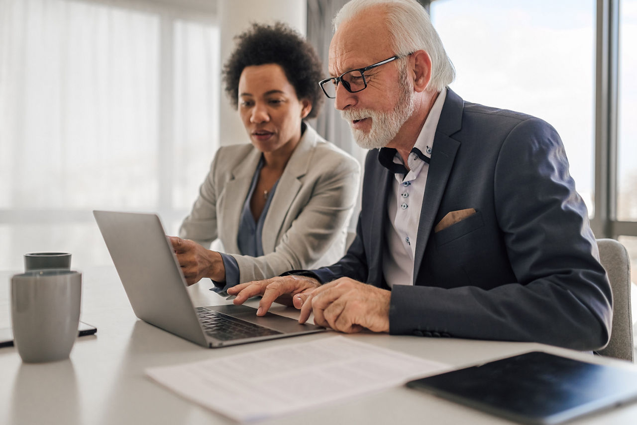 Focused male and female professionals planning business strategy on laptop. Business partners are analyzing plan during meeting. They are sitting at desk in office.