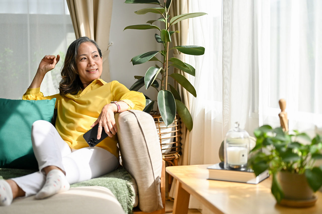 Portrait of a happy asian aged woman or retired woman resting in the modern living room, sitting on the comfortable sofa and looking through the window.