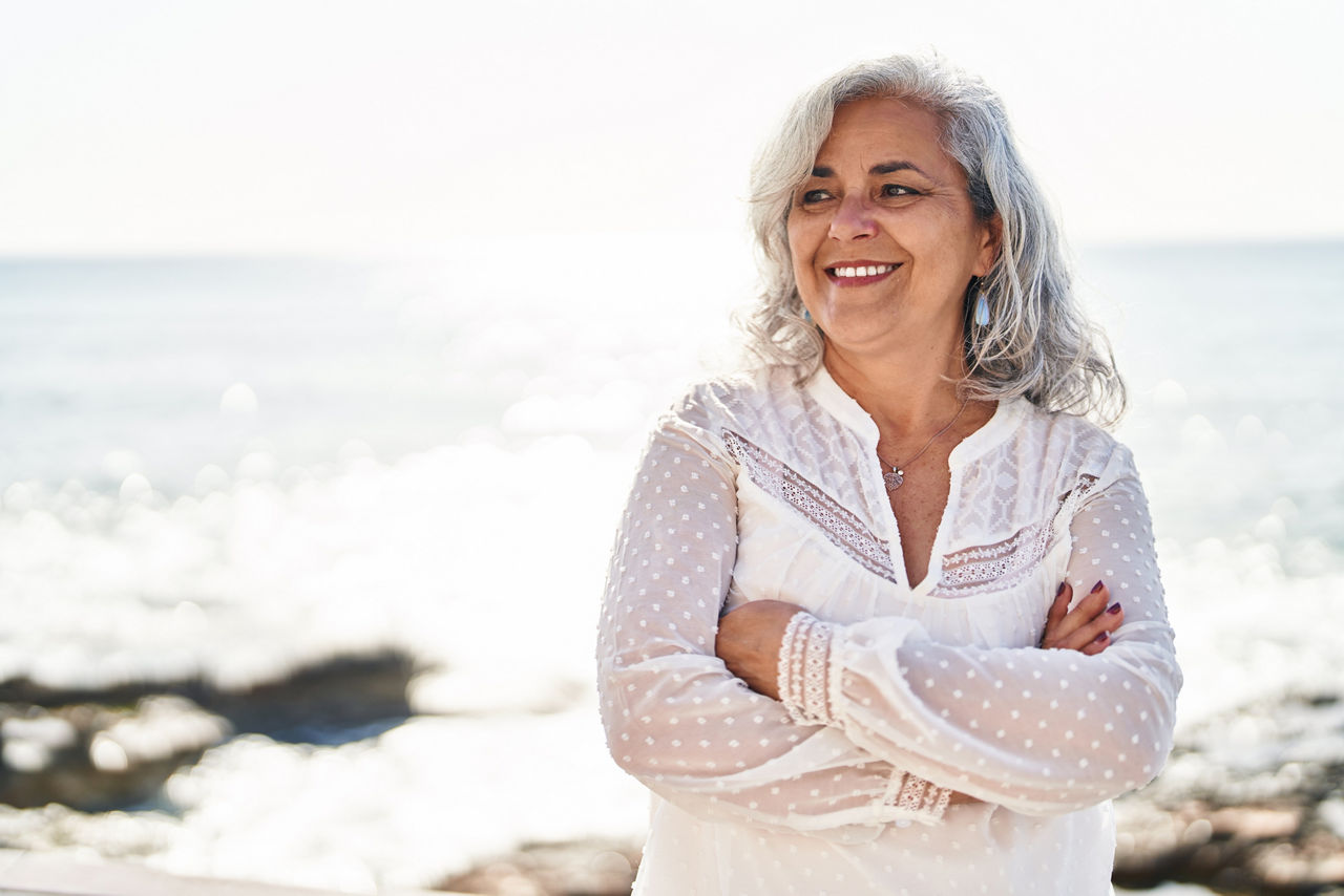 Middle age woman smiling confident standing with arms crossed gesture at seaside
