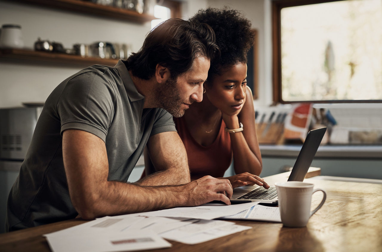 Couple with a laptop doing finance paper work, paying debt insurance loans or online ebanking together at home. Two serious people planning and looking at financial document, bills rate for mortgage.