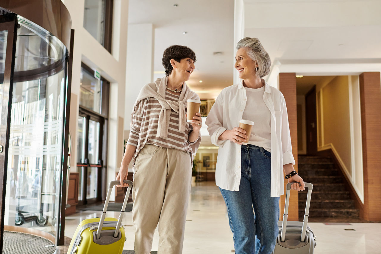 Senior lesbian couple, one holding luggage, the other holding hands, ready for adventure.