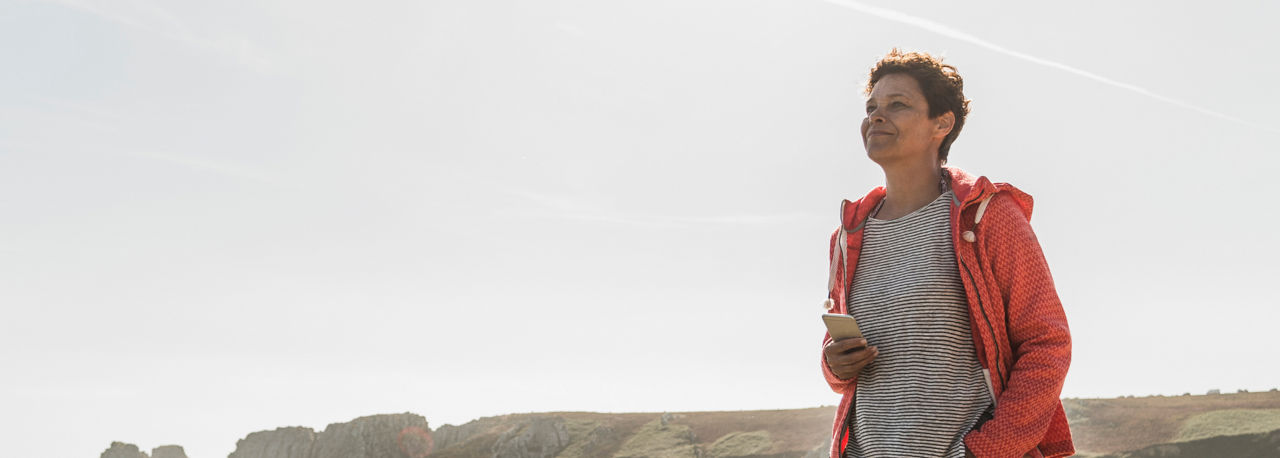 Woman walks along the coast as cliffs appear in the background. 