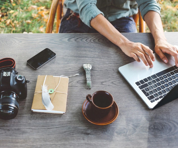 A photographer works on a laptop computer on a desk outside.