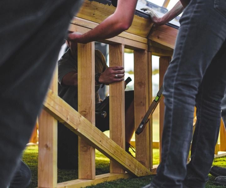 A group works together to assemble a complex wooden structure outside.