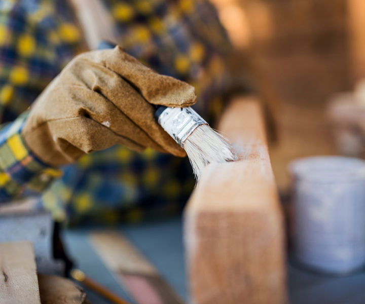 A hand in a work glove paints a wood board.