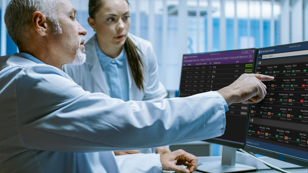 Doctors reviewing patient data on dual monitors in a hospital setting.