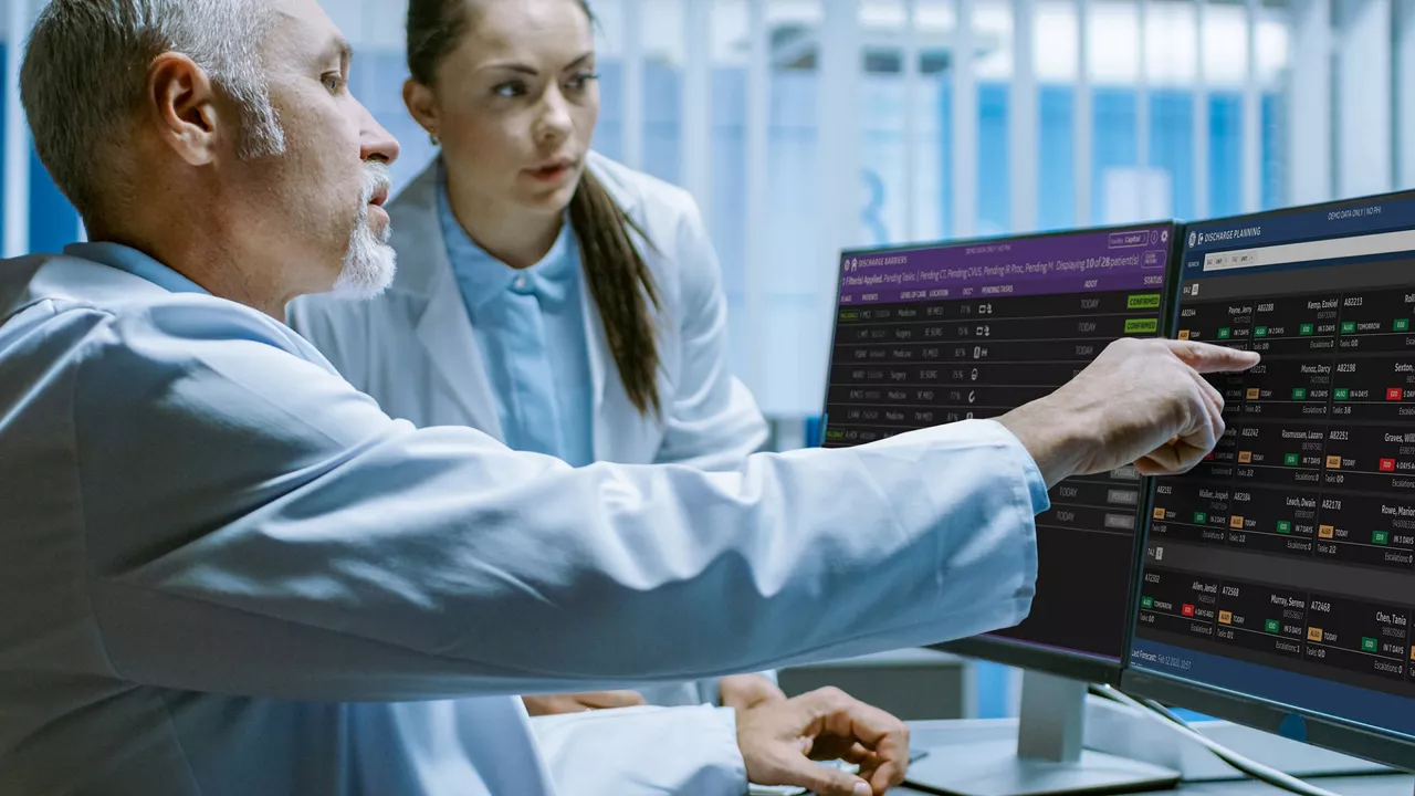 Doctors reviewing patient data on dual monitors in a hospital setting.