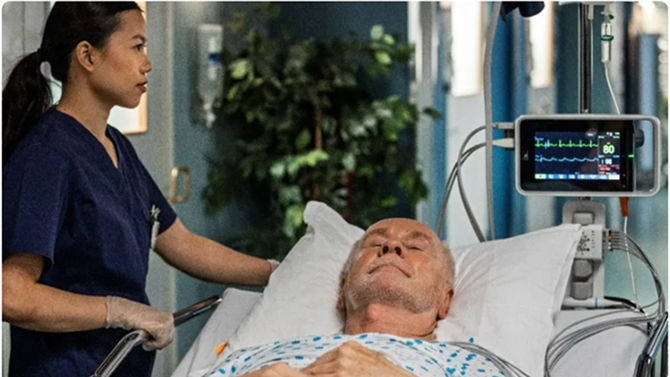 A nurse checks on a patient resting in a hospital bed while monitoring vital signs on a nearby display.