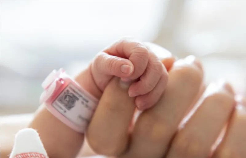 Crying infant being shown to their mother in an operating room.