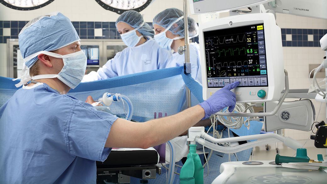 Two surgeons working on a patient and one surgeon interacting with a monitor.