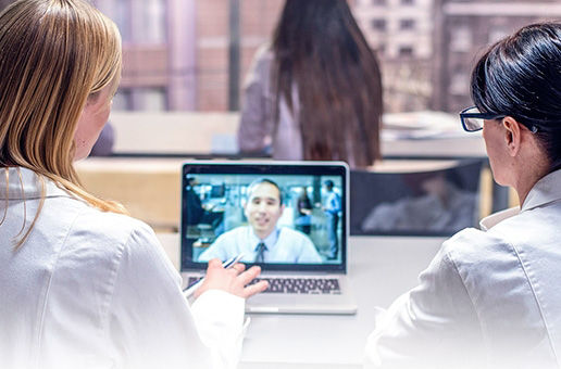 Two females in white lap coats looking a laptop screen with a man in a tie