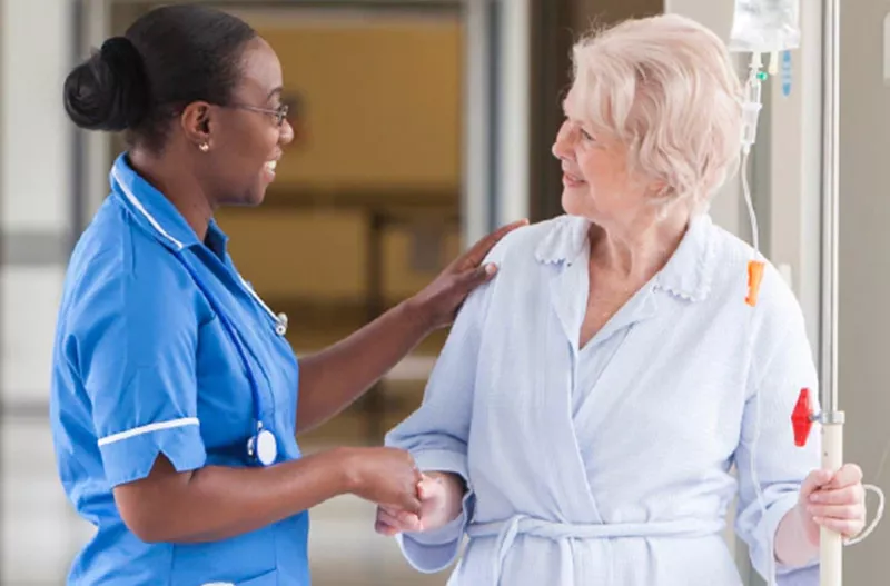 Middle-aged female nurse helping an elderly woman as she walks with her IV pole