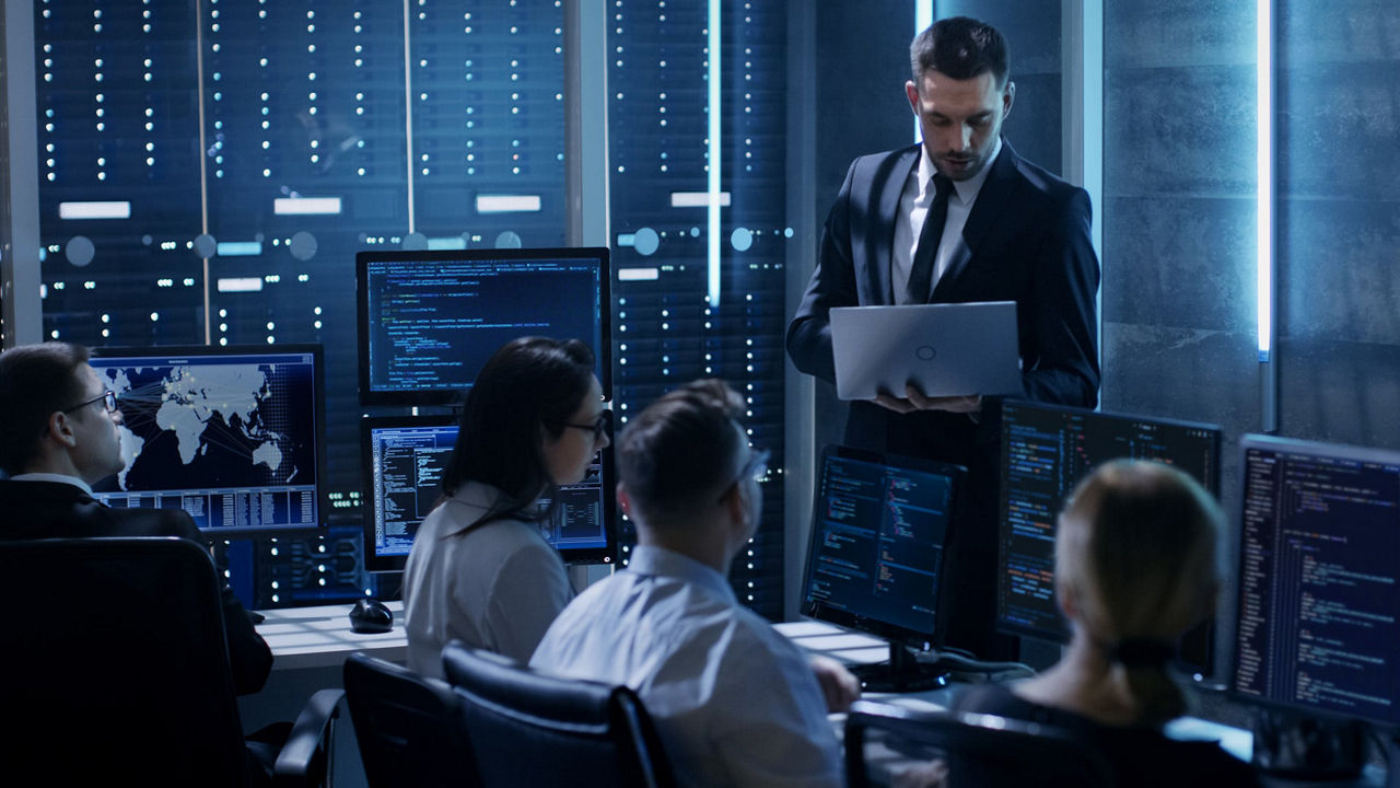 Person standing up holding a laptop holding a small group meeting in an IT environment