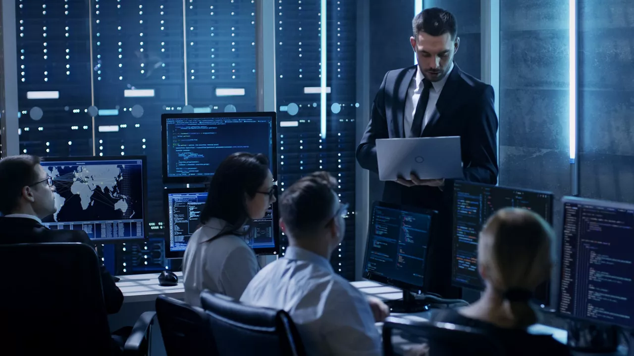 Person standing up holding a laptop holding a small group meeting in an IT environment