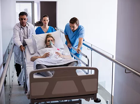 pregnant woman with an oxygen mask being wheel in a hospital bed by a doctor and two nurses