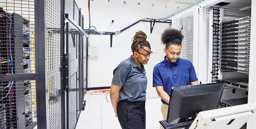 two technicians working on a computer in an equipment room