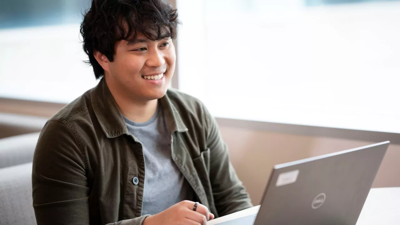 Employee sitting in a booth smiling and working on a laptop