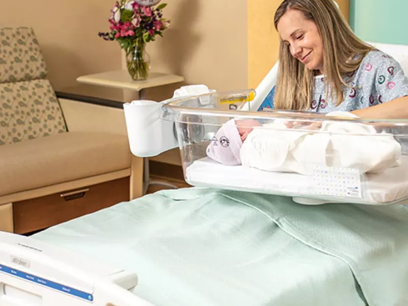 Woman on bed with newborn baby in clear medical casing