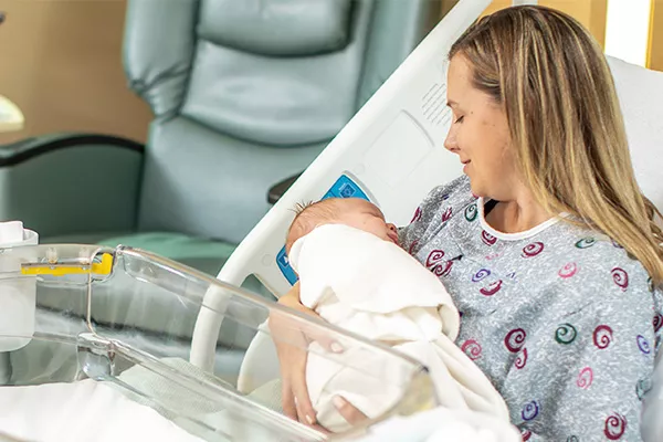 Mother in hospital bed holding newborn with HALO Bassinest on lap