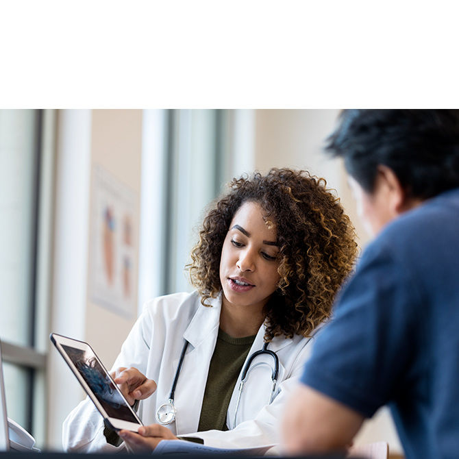 Female doctor with curly hair showing colleague something on tablet