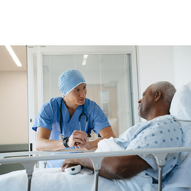 Cardiologist in surgical scrubs talking to male patient at bedside